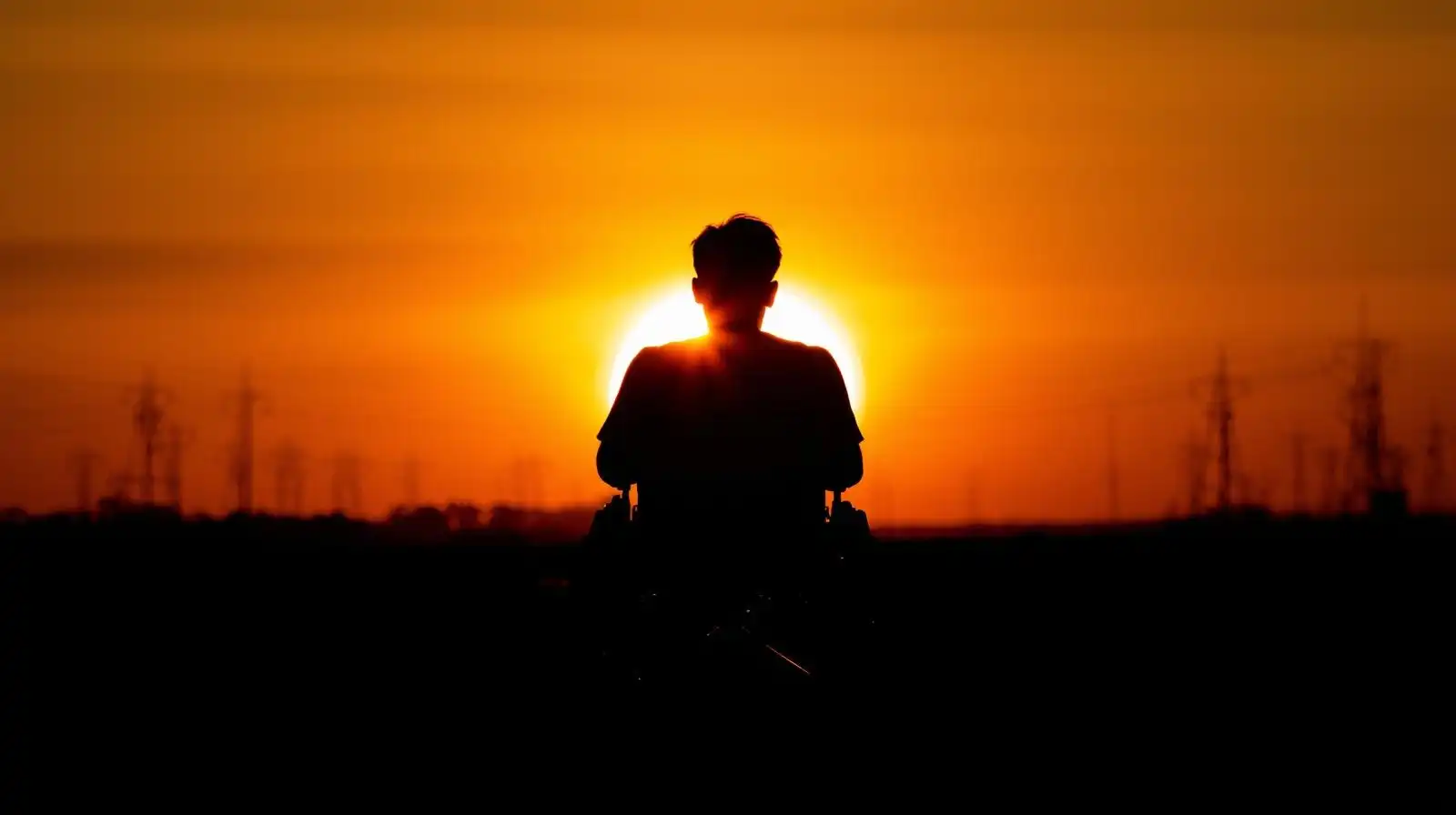Silhouette of man in wheelchair watching sunrise symbolizing new beginnings.